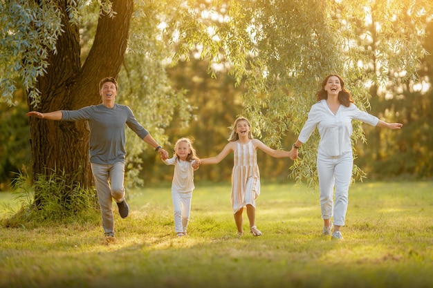 Glückliche Familie bei Sonnenuntergang Vater, Mutter und Kinder laufen, haben Spaß und genießen den Sommerabend