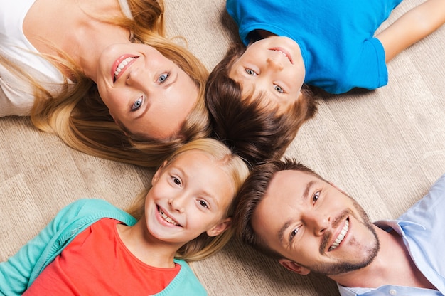 Glückliche Familie. Blick von oben auf die glückliche vierköpfige Familie, die sich miteinander verbindet und lächelt, während sie auf dem Holzboden liegt