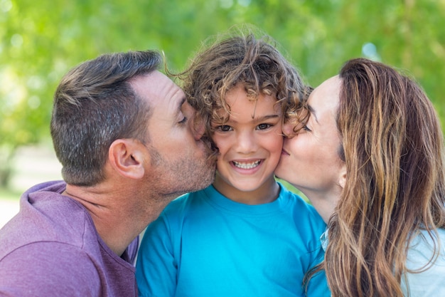 Glückliche Familie, die an der Kamera im Park an einem sonnigen Tag küsst