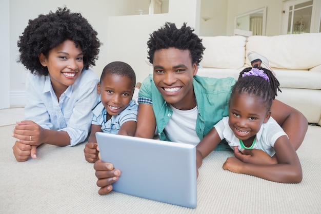 Glückliche Familie, die auf dem Boden unter Verwendung der Tablette liegt