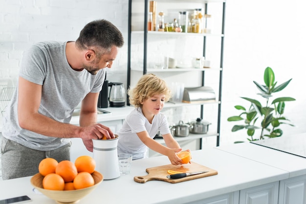 glückliche familie, die frischen orangensaft mit einer presse auf dem tisch in der küche macht