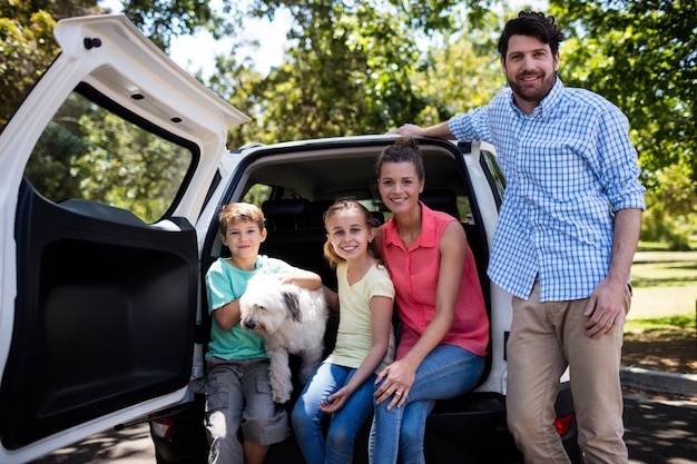 Glückliche Familie, die im Autokofferraum mit ihrem Hund sitzt