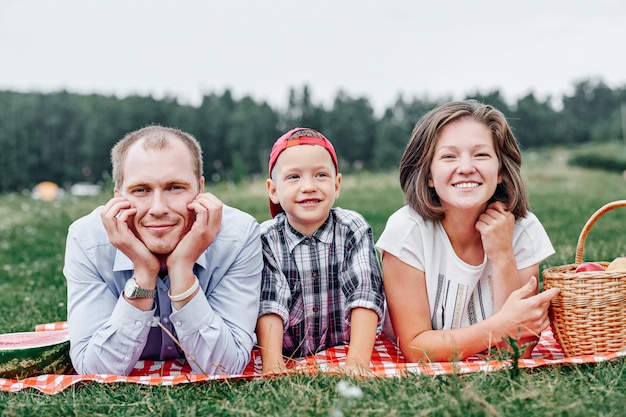 Glückliche Familie, die in der Natur ruht. Mutter, Vater und Kind Genießen und liegen auf kariertem Plaid auf der Wiese