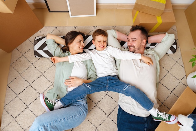 Glückliche Familie, die in einem neuen Zuhause auf dem Boden liegt, mit Cordboard-Boxen herum