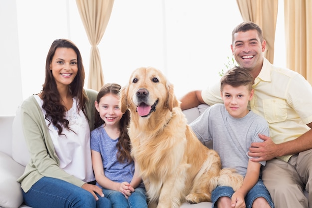 Glückliche Familie, die mit goldenem Apportierhund auf Sofa sitzt