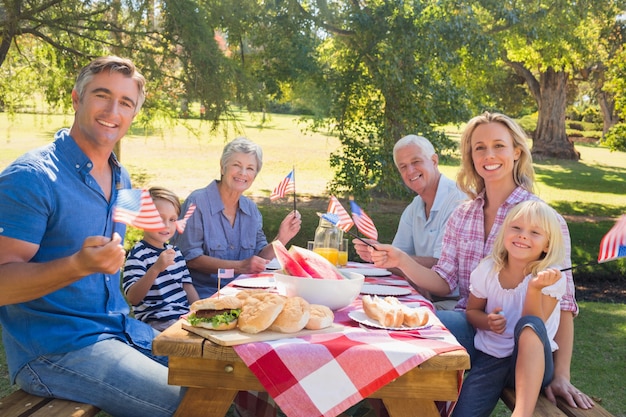 Glückliche Familie, die Picknick hat und amerikanische Flagge hält