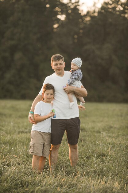 Glückliche Familie, die sich auf einem Sommerspaziergang umarmt und umarmt. Vater und seine beiden Söhne gehen im Park spazieren und genießen die wunderschöne Natur. Niedliches Familienporträt