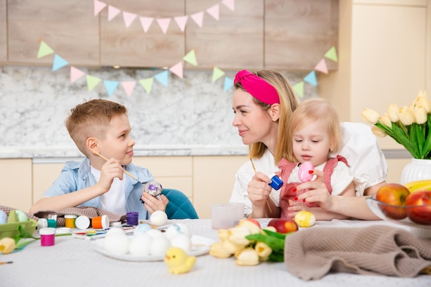 Glückliche Familie, die sich auf Ostern vorbereitet Niedliche Kinder mit Mutter, die Eier malt Heimaktivität Konzept der Einheit und Liebe Mutter, Sohn, Tochter, Bruder und Schwester