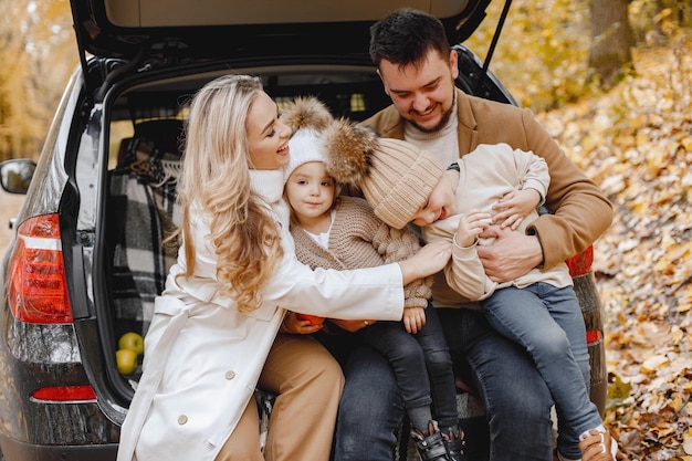 Glückliche Familie, die sich nach einem Tag im Freien im Herbstpark ausruht. Vater, Mutter und zwei Kinder sitzen im Kofferraum und lächeln. Familienurlaub und Reisekonzept.