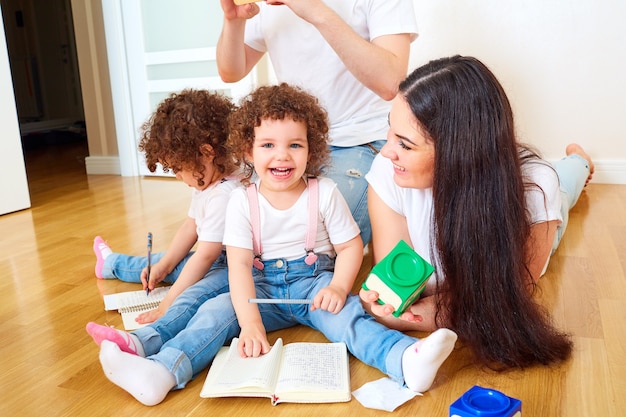 Glückliche Familie, die Spaß auf dem Boden im Zimmer hat Mama Papa und Tochter Mädchen lachen beim Schreiben in einem Notizbuch