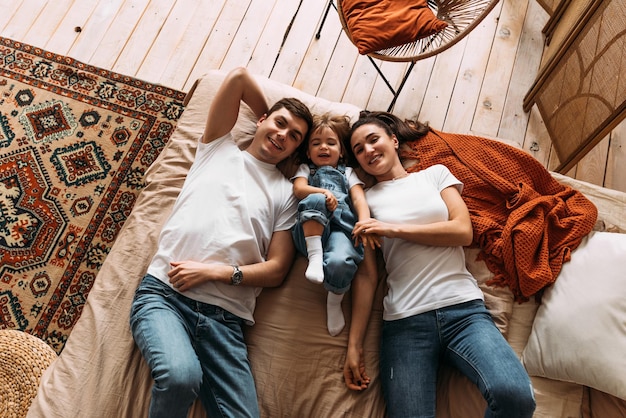 Glückliche Familie, die Spaß im Schlafzimmer hat, während sie auf dem Bett liegen Glückliche junge Familie Glückliche Familie, die im Schlafzimmer mit glücklicher und lächelnder Draufsicht auf dem Bett liegt Konzept der Familienbeziehungen Stock Foto