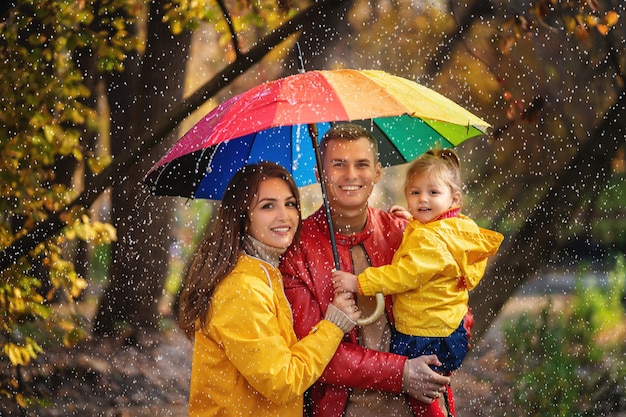 Glückliche Familie, die unter den Regen am Herbstpark geht