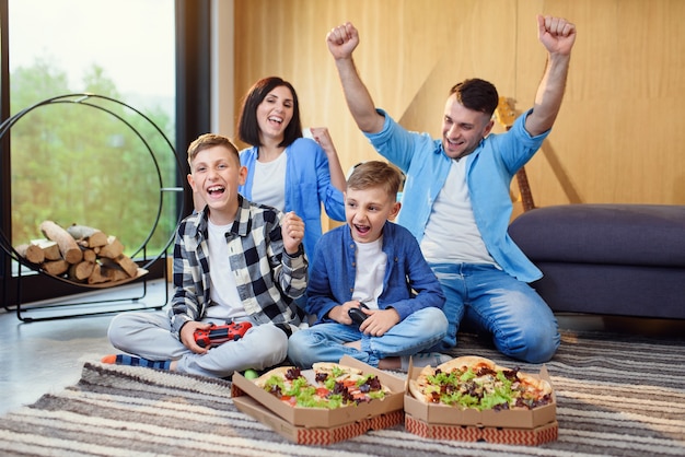 Glückliche Familie, die Videospiele mit Gamepads spielt und leckere Pizza isst