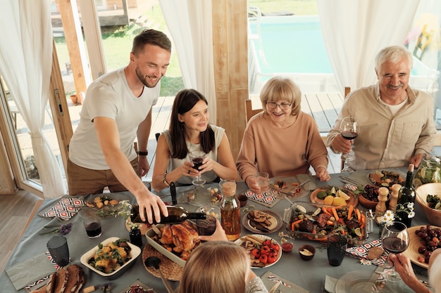 Glückliche Familie, die Wein trinkt und köstliche Gerichte isst, während sie am Tisch sitzen und gemeinsam Urlaub feiern
