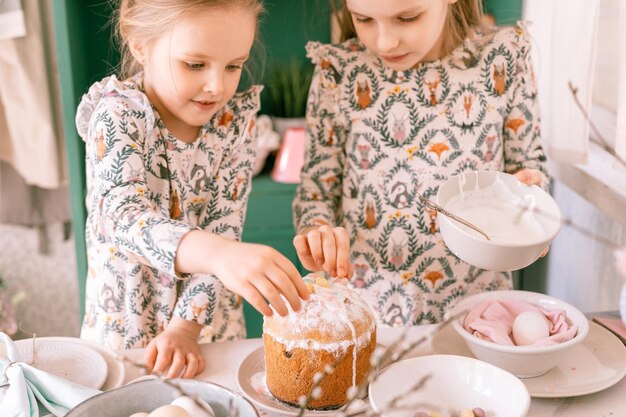 Glückliche Familie, ehrliche kleine Kinder, Schwestern, Mädchen, zusammen haben Spaß bereit, Frühlings-Osterferien zu Hause in der Küche zu dekorieren, Tisch und Osterkuchen, Bäckerei, süße Glasur und Süßigkeiten zum Mittag- oder Abendessen