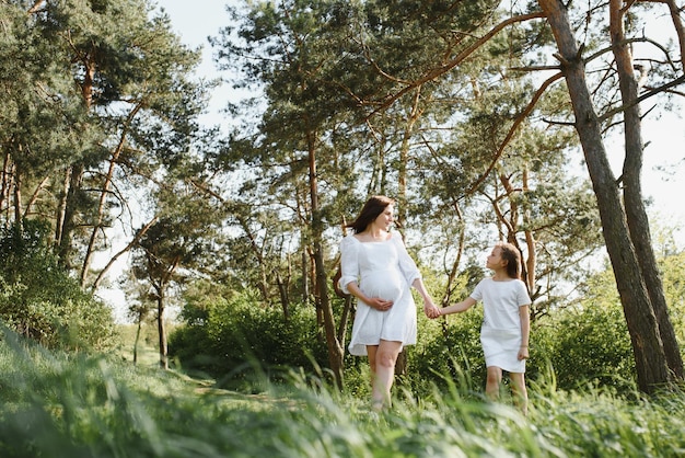 Glückliche Familie eine junge schöne schwangere Frau mit ihrer kleinen süßen Tochter an einem sonnigen Sommertag Beziehung zwischen Eltern und Kindern Natur auf dem Land