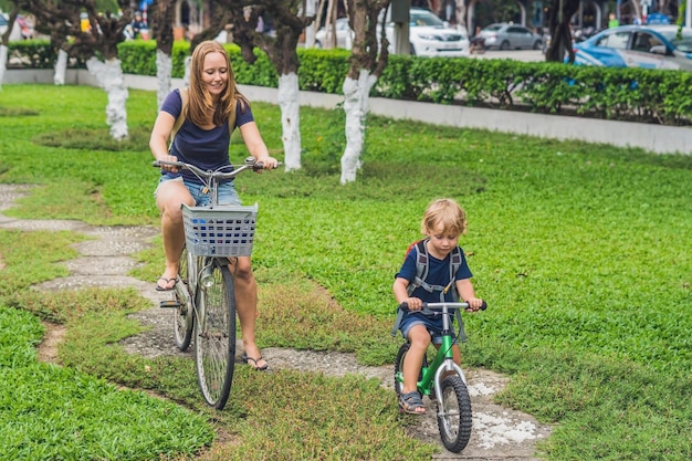 Glückliche Familie fährt draußen Fahrrad und lächelt. Mama auf einem Fahrrad und Sohn auf einem Laufrad.