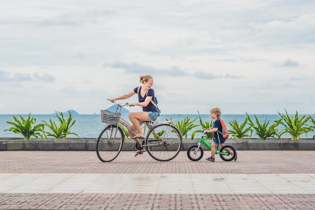 Glückliche Familie fährt draußen Fahrrad und lächelt. Mama auf einem Fahrrad und Sohn auf einem Laufrad.