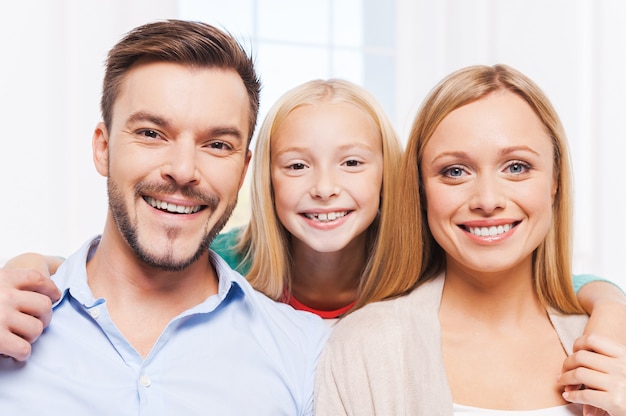 Glückliche Familie. Glückliche dreiköpfige Familie, die sich miteinander verbindet und lächelt, während sie drinnen sitzt