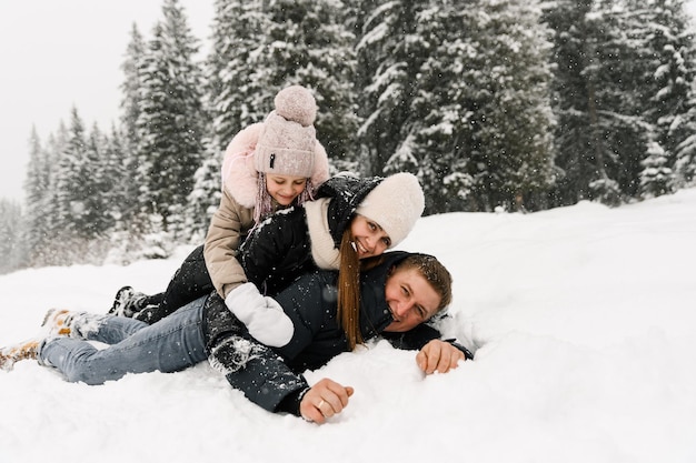 Glückliche Familie hat Spaß im Winterwald. Mutter, Vater und Tochter liegen am Boden und spielen mit Schnee. Familienkonzept. Genießen Sie die gemeinsame Zeit