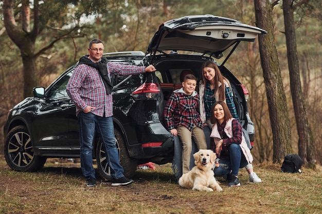 Glückliche Familie hat Spaß mit ihrem Hund in der Nähe eines modernen Autos im Freien im Wald