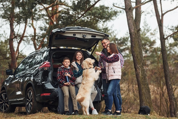 Glückliche Familie hat Spaß mit ihrem Hund in der Nähe eines modernen Autos im Freien im Wald