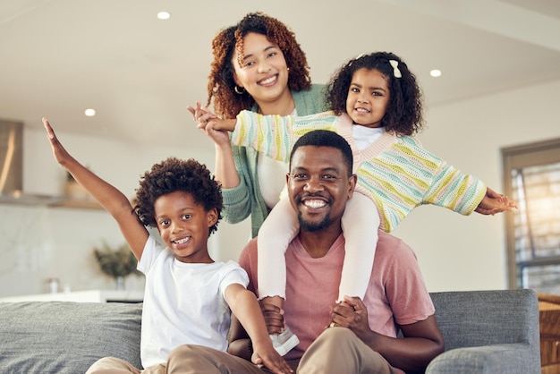 Glückliche Familie huckepack und Porträt von Kindern mit Eltern auf einem Sofa, die lächeln und fröhlich sind, während sie in ihrem Zuhause Freundschaft schließen. Flugzeugspaß und Gesicht von Kindern mit Mutter und Vater zusammen im Wohnzimmer