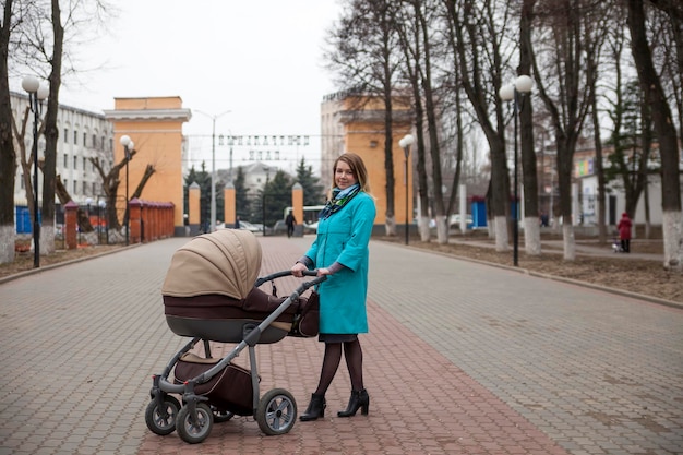 Glückliche Familie im Freien junge Mutter geht mit kleinem Baby im Kinderwagen in der Frühlingsstadt spazieren