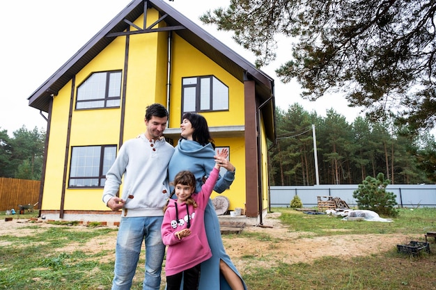 Glückliche Familie im Hof eines unvollendeten Hauskaufs eines Hüttenhypothekendarlehens-Umzugsbaus