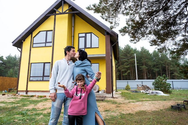 Glückliche Familie im Hof eines unvollendeten Hauskaufs eines Hüttenhypothekendarlehens-Umzugsbaus