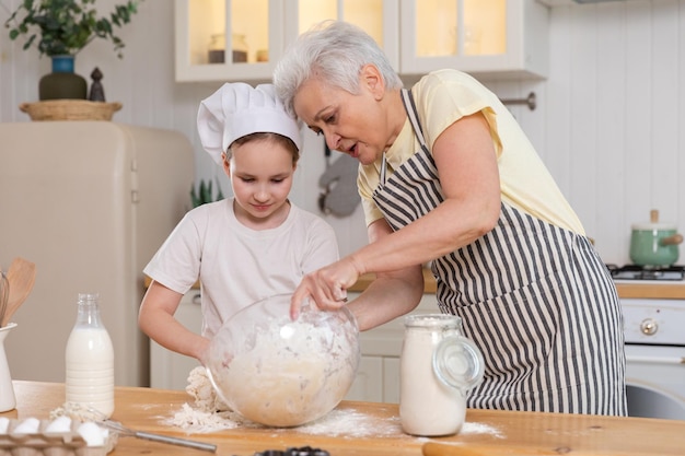 Glückliche Familie in der Küche. Großmutter und Enkelin kochen gemeinsam in der Küche. Oma bringt einem kleinen Mädchen bei, Teig zu kneten, Kekse zu backen. Teamarbeit im Haushalt hilft Familiengenerationen beim Konzept