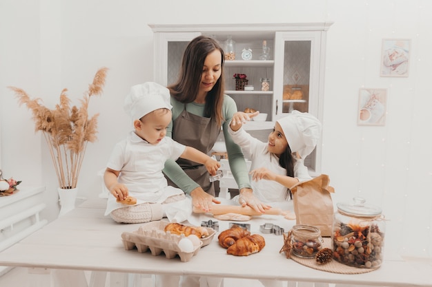 Glückliche Familie in der Küche. Mama und Kinder in Kochkostümen in der Küche. Mama und Kinder bereiten Teig vor, backen Kekse