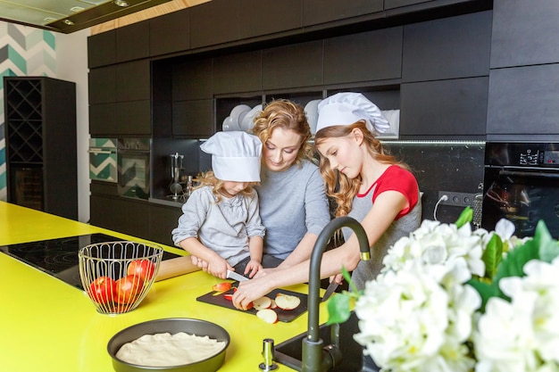 Glückliche Familie in der Küche Mutter und zwei Kinder bereiten Teig zu backen Apfelkuchen Mutter und Töchter gurren