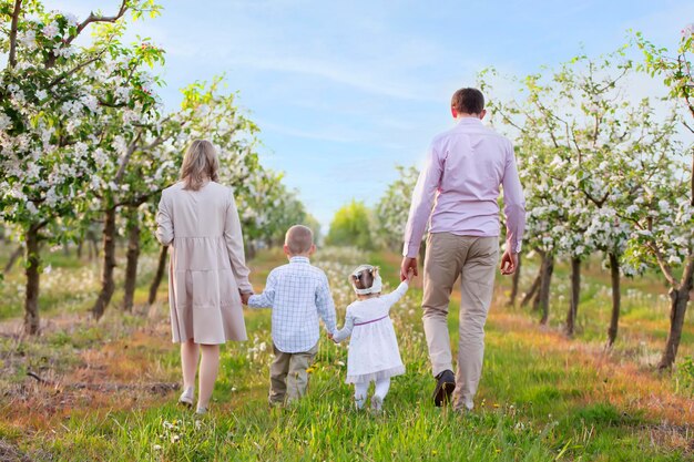 Glückliche Familie in einem blühenden GartenMama Papa und Kinder gehen die Straße des Frühlingsgartens entlang