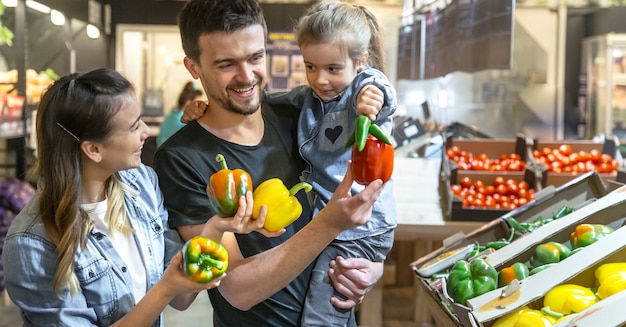 Glückliche Familie kauft Gemüse. Fröhliche dreiköpfige Familie, die Papiere in der Gemüseabteilung auswählt.