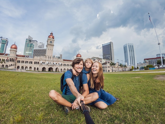 Glückliche Familie macht Selfie auf dem Hintergrund des Merdeka-Platzes und des Sultan Abdul Samad-Gebäudes. Reisen mit Kindern Konzept