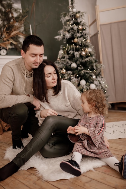 Glückliche Familie, Mama, Papa und kleine Tochter in der Nähe von Weihnachtsbaum und Kamin zu Hause.