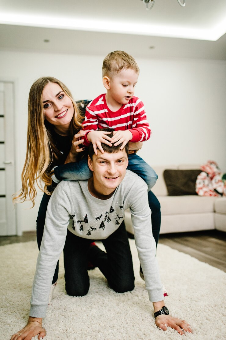 Foto glückliche familie: mama, papa und kleiner sohn in weihnachtsmann-pullovern spielen auf dem boden. liebe umarmungen genießen, urlaub menschen. zusammengehörigkeitskonzept.