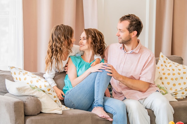 Glückliche Familie, Mama Papa und Tochter sitzen auf der Couch und lachen zusammen