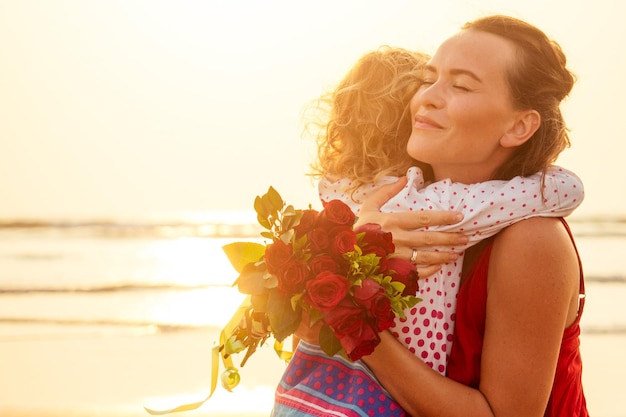Glückliche Familie mit Blumenstrauß Rosen am Strand am Meer bei Sonnenuntergang
