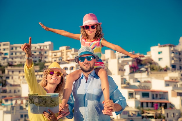 Glückliche Familie mit bunten Sonnenbrillen und Hüten, die eine Karte mit einer europäischen Stadt im Hintergrund halten