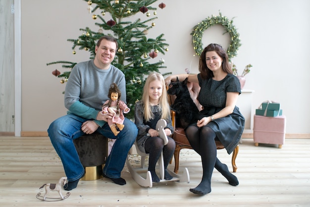 Glückliche Familie mit dem Hund, der Kamera im Raum mit cristmas Baum- und des neuen Jahresdekorationen lächelt und betrachtet