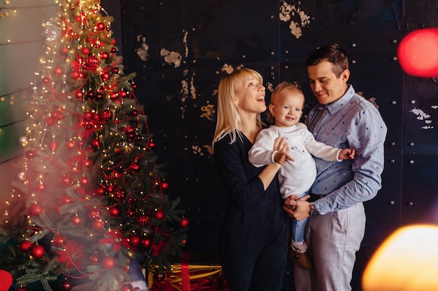 Glückliche Familie mit einem Kind feiert das neue Jahr in der Nähe des Weihnachtsbaumes