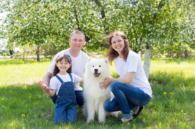 Glückliche Familie mit einem weißen Hund in einem Sommerpark.