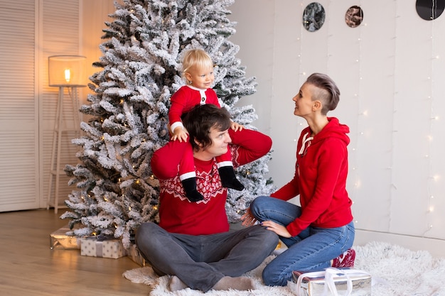 Glückliche Familie mit Geschenken im Zimmer. Frohe Weihnachten und schöne Feiertage. Eltern und ihr kleiner Kinderjunge, der drinnen Spaß hat.