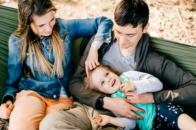 Glückliche Familie mit Kind, das in der Hängematte im Freien entspannt.