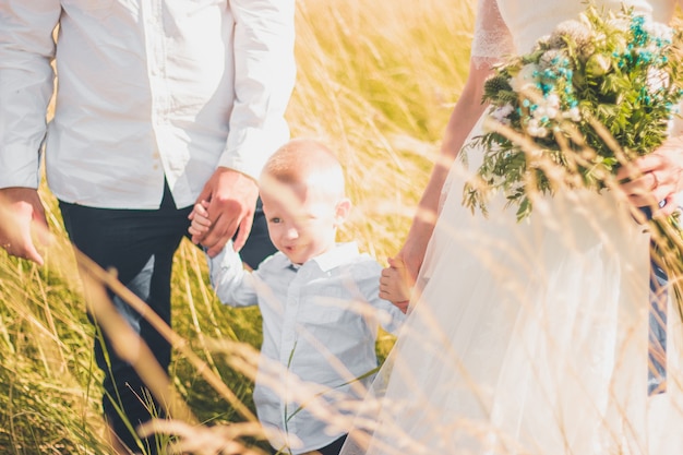 Glückliche Familie mit Kind, die an einem warmen und sonnigen Sommertag zusammen im Weizenfeld spazieren geht. Weicher Fokus.