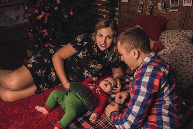 Glückliche Familie mit Kind feiert Neujahr und Weihnachten am geschmückten Weihnachtsbaum und Girlanden