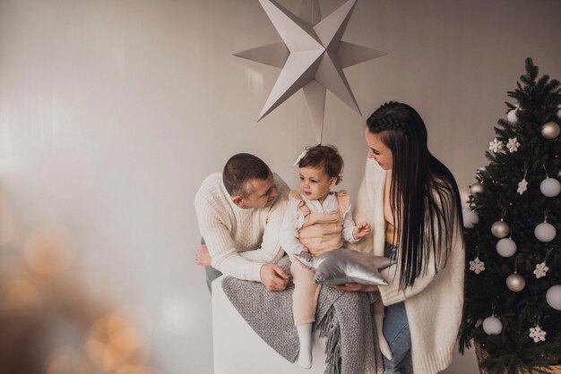 Glückliche Familie mit Kind feiert Neujahr und Weihnachten am geschmückten Weihnachtsbaum und Girlanden