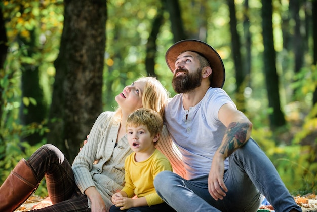 Glückliche Familie mit Kind Junge entspannen beim Wandern im Wald Familienwochenende Mutter, Vater und kleiner Sohn sitzen Waldpicknick Guten Tag für Frühlingspicknick in der Natur Vereint mit der Natur Familientag-Konzept